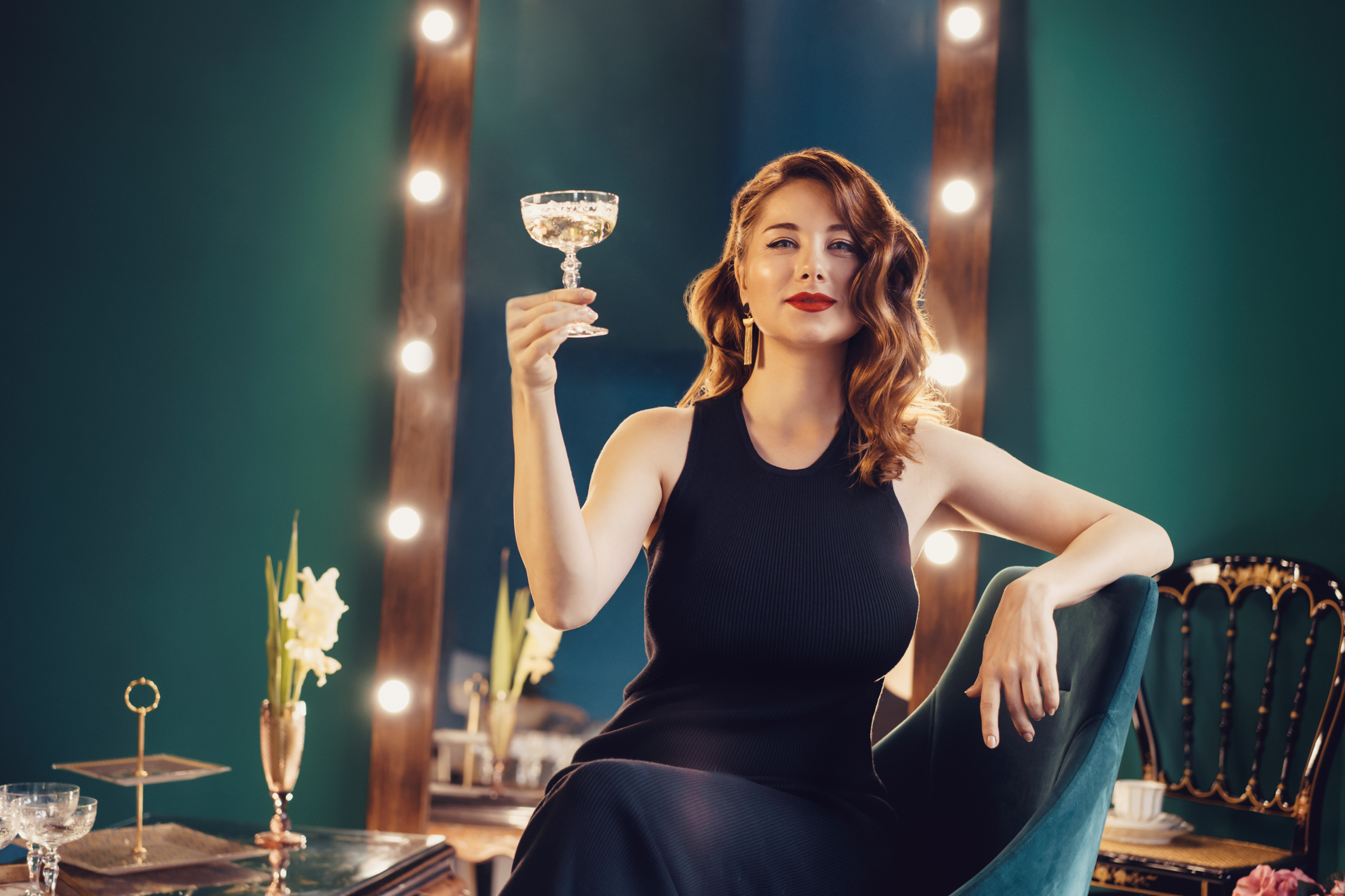 Posh elegant woman in evening dress with a glass of champagne in the luxury dressing room interior. Celebrity, superstar lifestyle. Party, drinks, holidays and celebration concept. Selective focus.